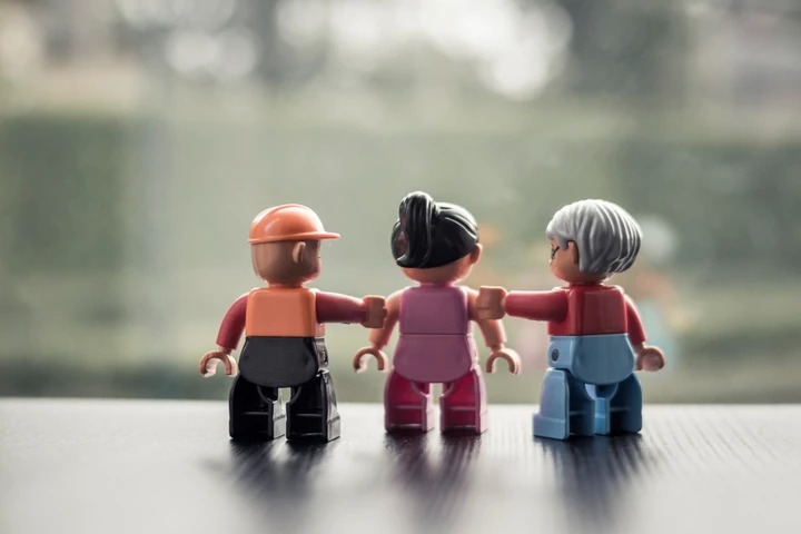 Drie Lego-figuren van verschillende generaties, gearmd naast elkaar